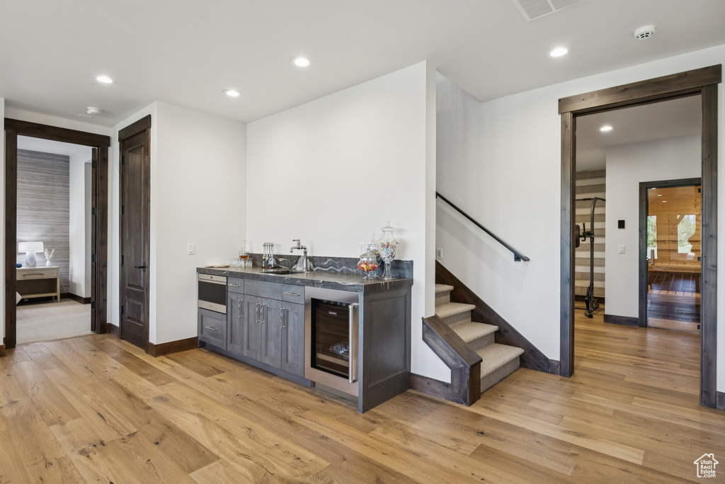Indoor wet bar featuring wine cooler, stairs, light wood finished floors, baseboards, and recessed lighting