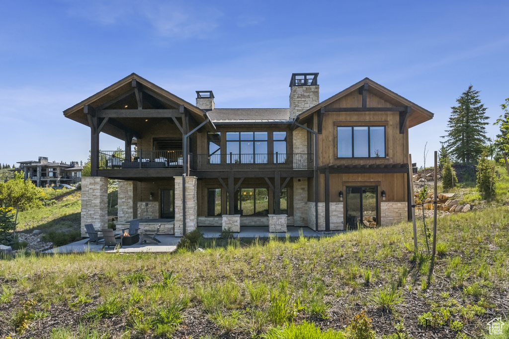 Back of house with stone siding, a patio area, a chimney, and a balcony