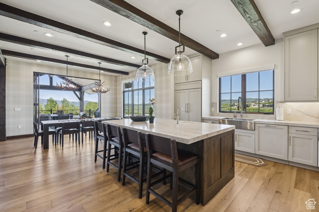 Kitchen with a sink, light wood-style floors, an island with sink, a kitchen bar, and light stone countertops