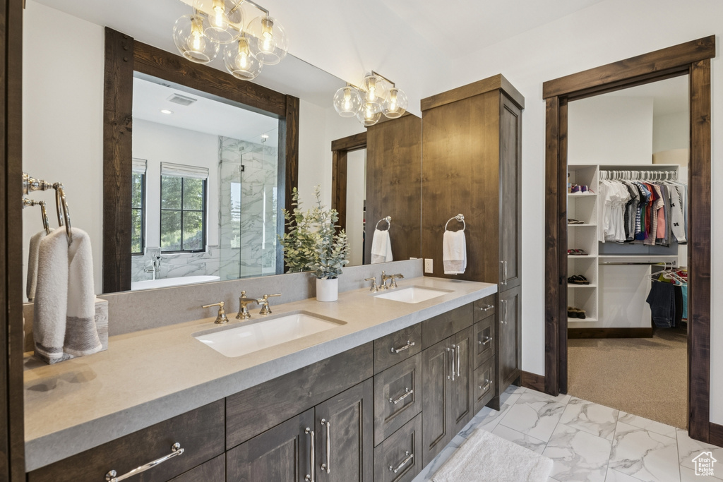 Full bath featuring double vanity, a walk in closet, marble look tiles, a shower, and a chandelier
