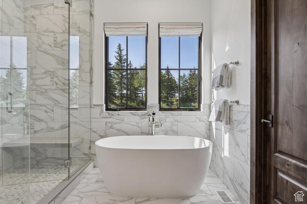 Full bath featuring a freestanding tub, marble finish flooring, a marble finish shower, and tile walls