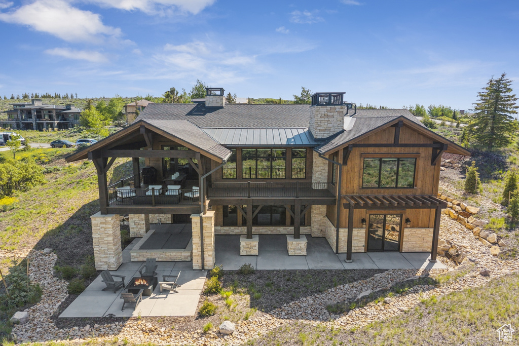 Rear view of property featuring stone siding, a standing seam roof, a patio area, a chimney, and an outdoor fire pit