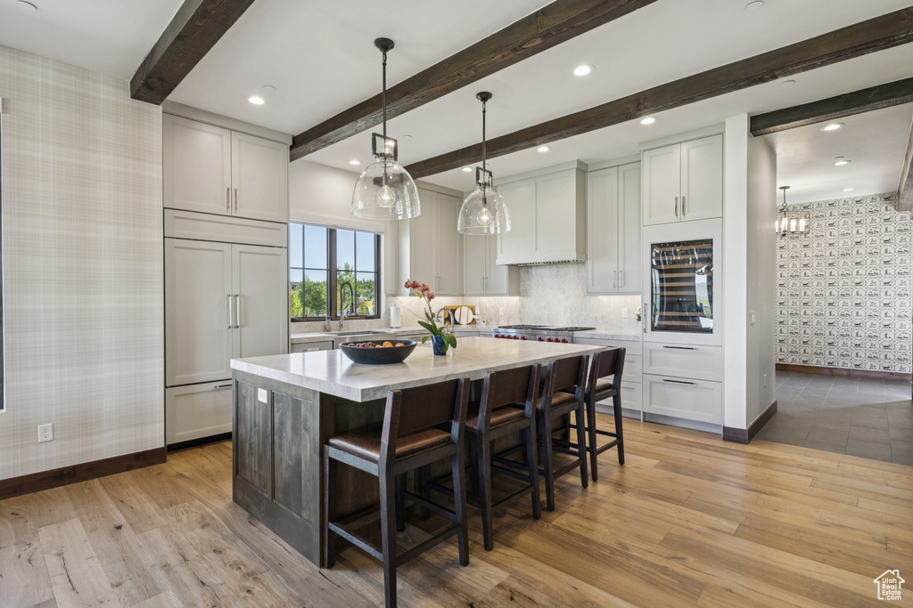 Kitchen with wallpapered walls, paneled refrigerator, baseboards, light wood-style floors, and a center island