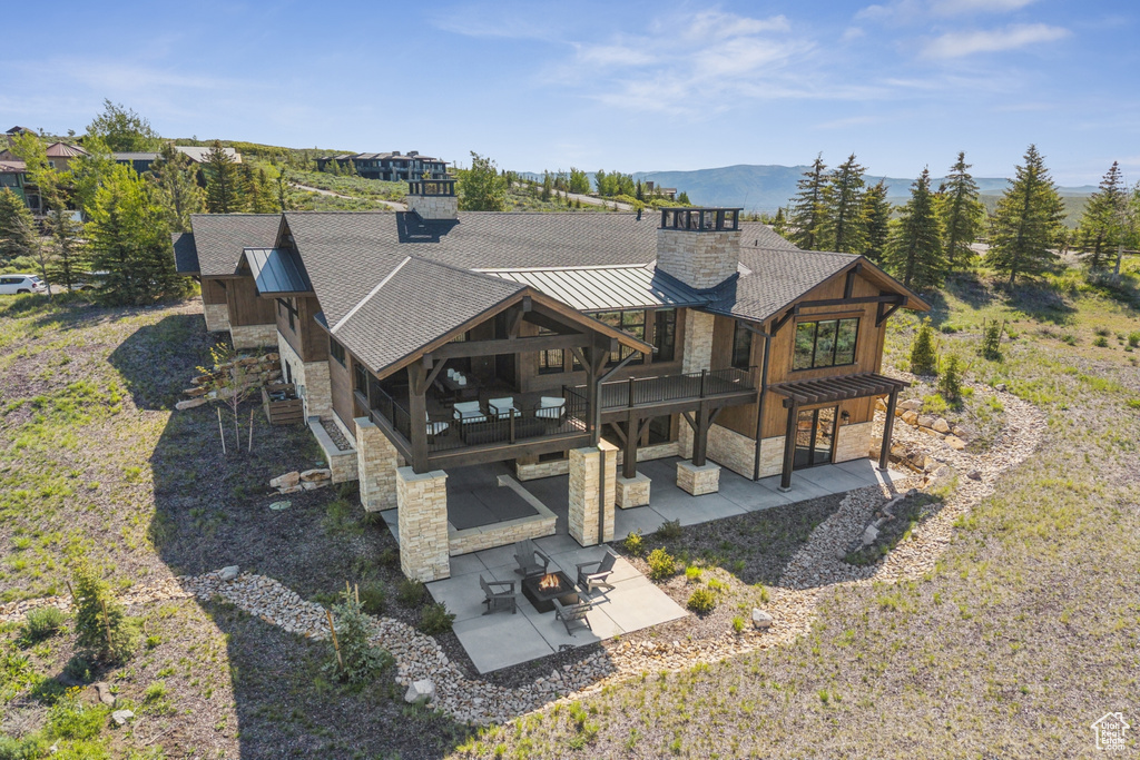 Back of house with stone siding, a chimney, a patio, a standing seam roof, and metal roof