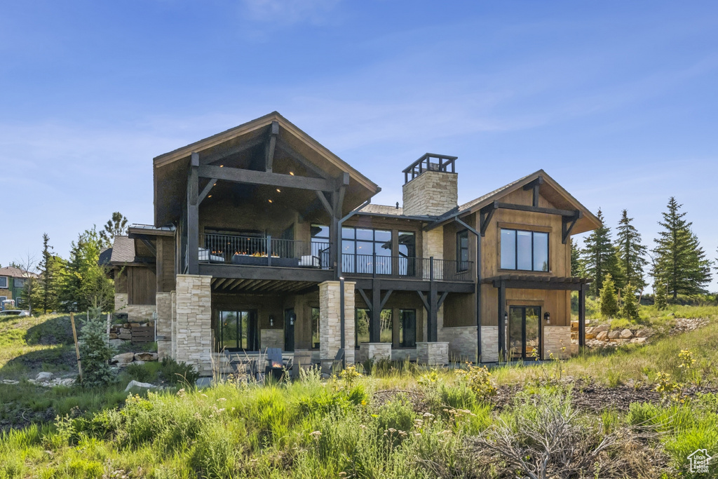 Rear view of property featuring stone siding, a balcony, and a chimney