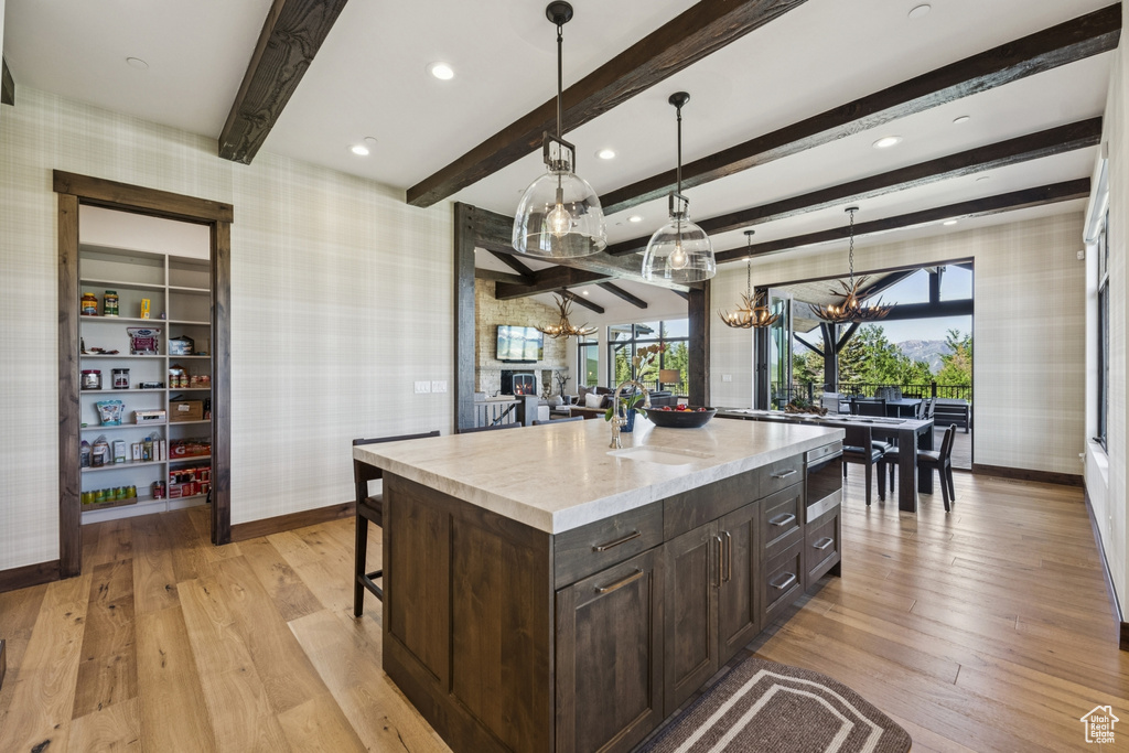 Kitchen with wallpapered walls, baseboards, a chandelier, light wood-style flooring, and beamed ceiling