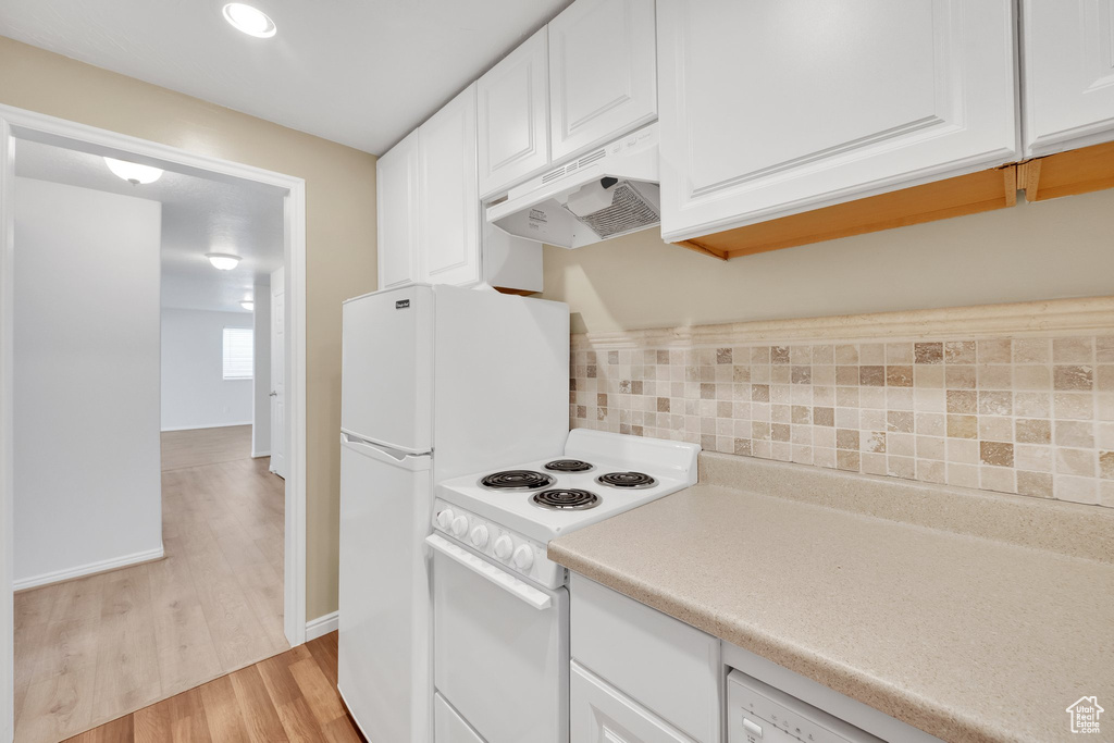 Kitchen with under cabinet range hood, white range with electric cooktop, white cabinets, light countertops, and light wood-style floors