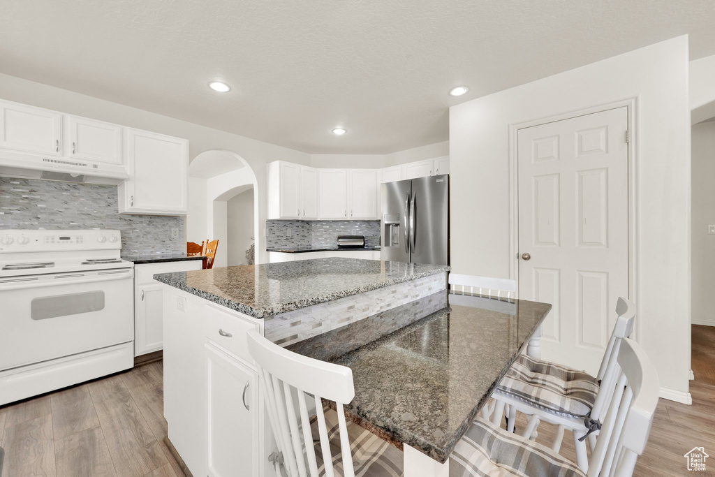 Kitchen featuring white range with electric cooktop, stainless steel refrigerator with ice dispenser, under cabinet range hood, a kitchen island, and a breakfast bar