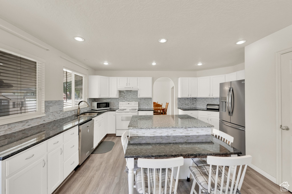 Kitchen with stainless steel appliances, a sink, a center island, a kitchen bar, and light wood finished floors