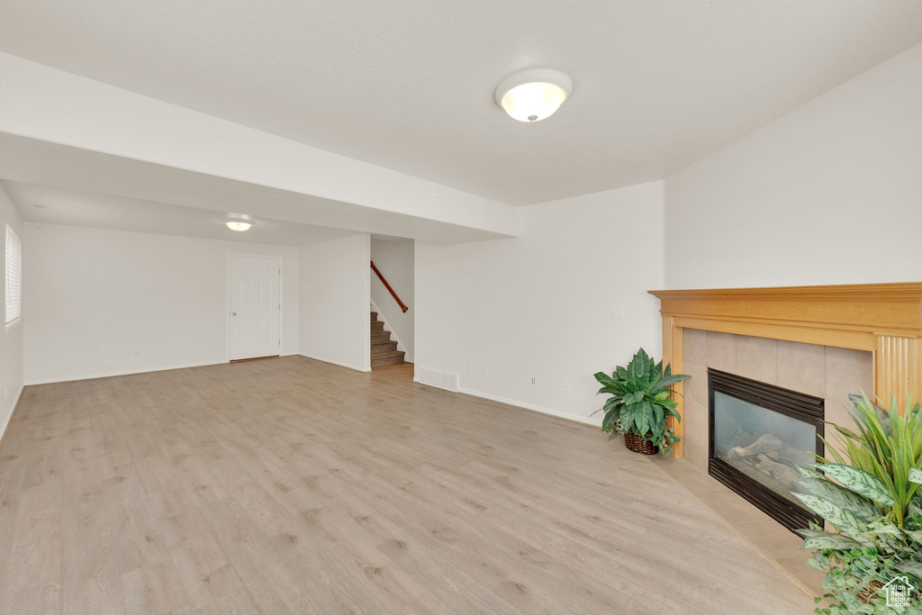 Unfurnished living room featuring wood finished floors, stairway, a tile fireplace, and baseboards