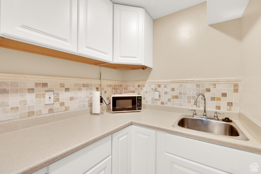 Kitchen with black microwave, a sink, white cabinets, and backsplash