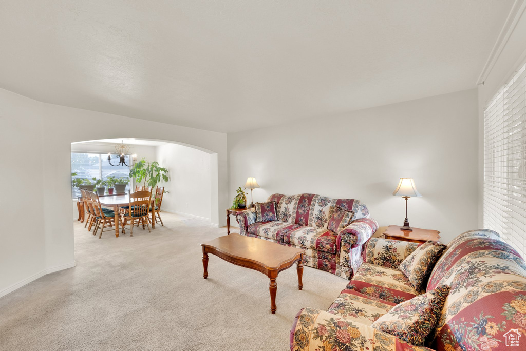 Living area with arched walkways, light colored carpet, plenty of natural light, and a chandelier