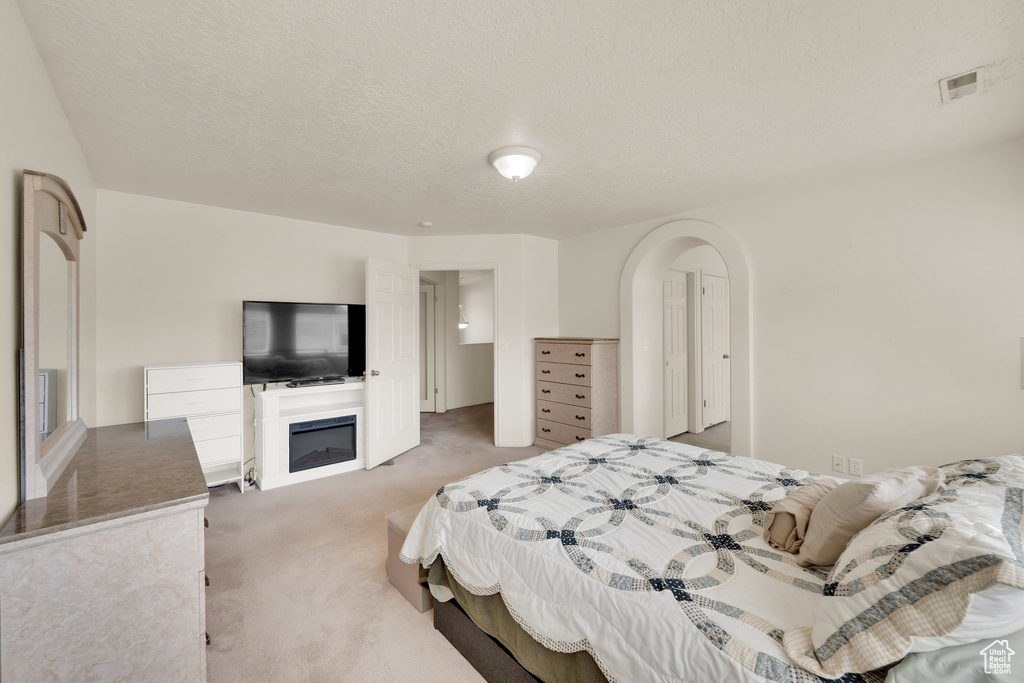 Bedroom featuring light colored carpet, a textured ceiling, and arched walkways