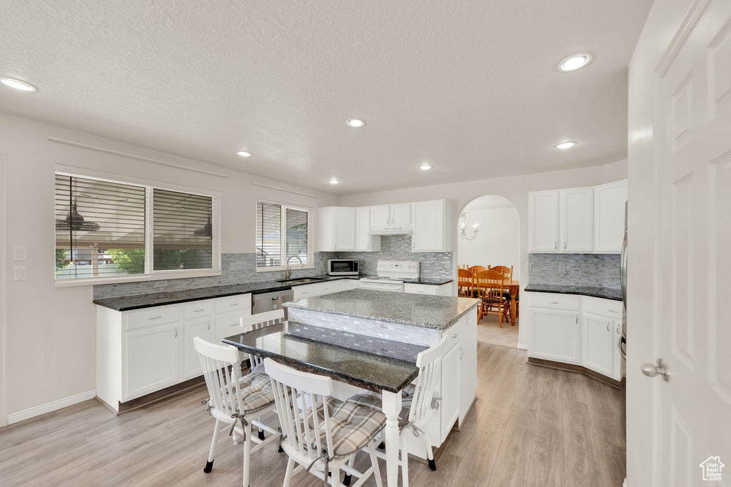 Kitchen with stainless steel appliances, arched walkways, tasteful backsplash, light wood-type flooring, and recessed lighting