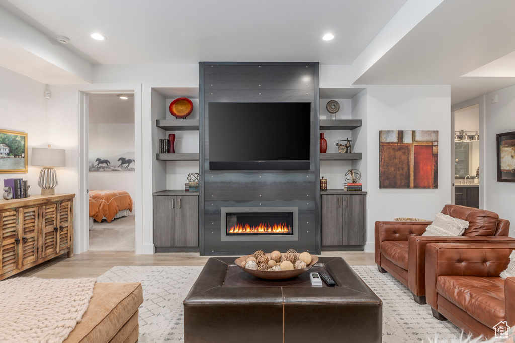 Living area with a large fireplace, light wood finished floors, recessed lighting, and built in shelves