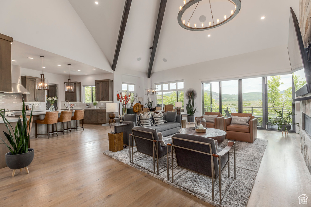Living room with a chandelier, high vaulted ceiling, light wood finished floors, a fireplace, and beam ceiling