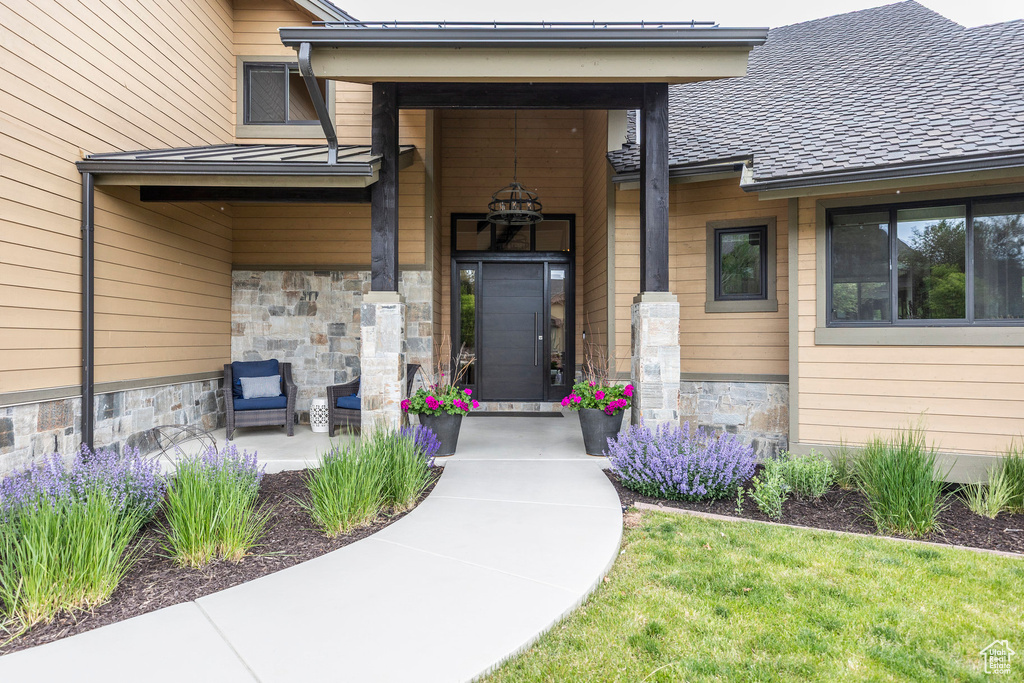 View of exterior entry with stone siding, a shingled roof, and covered porch