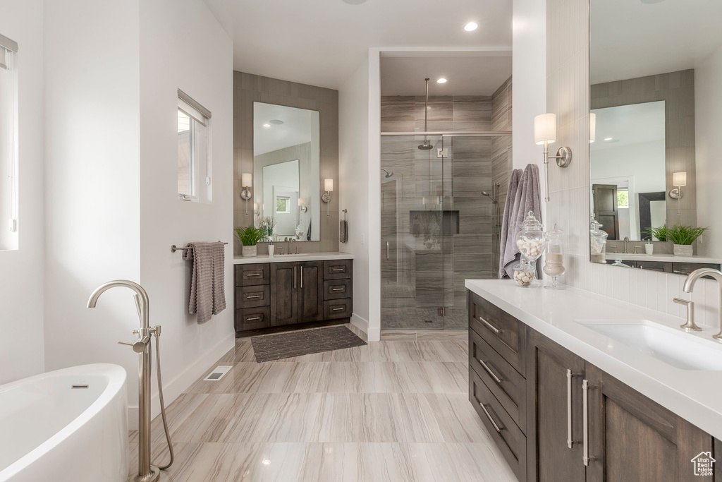 Bathroom with a stall shower, two vanities, a freestanding tub, and baseboards