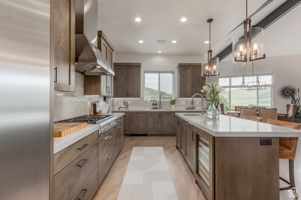 Kitchen with a chandelier, wall chimney exhaust hood, stainless steel appliances, a sink, and a breakfast bar