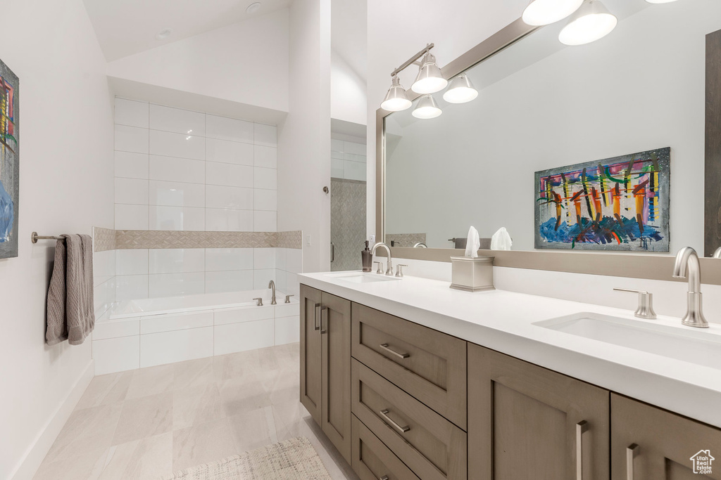Full bathroom featuring double vanity, tiled bath, and lofted ceiling