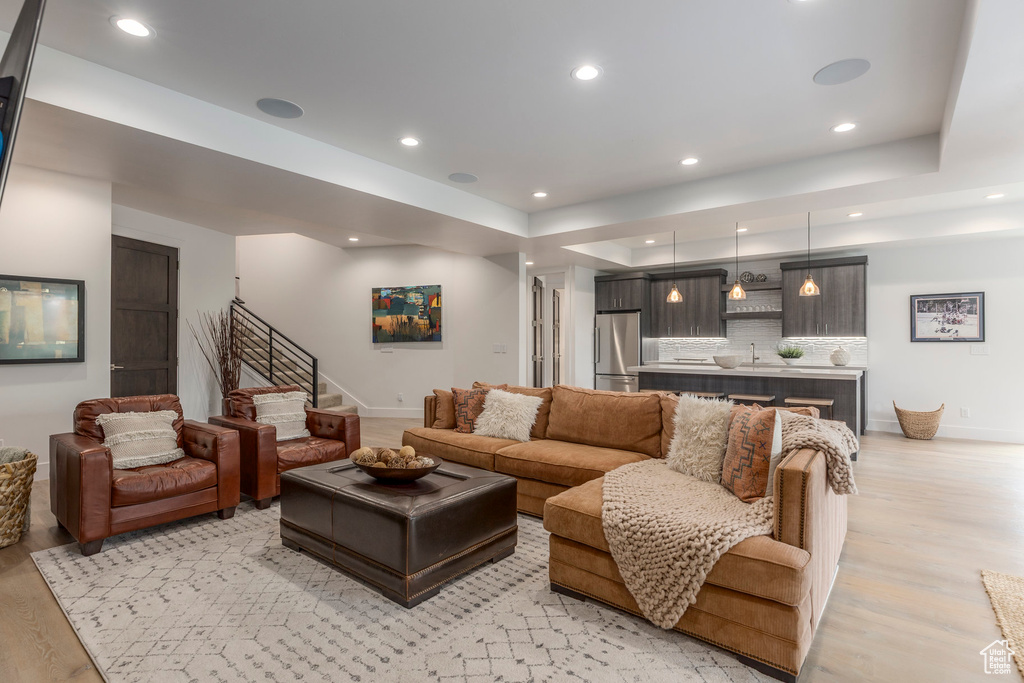 Living area featuring light wood-style flooring, baseboards, stairway, recessed lighting, and a tray ceiling