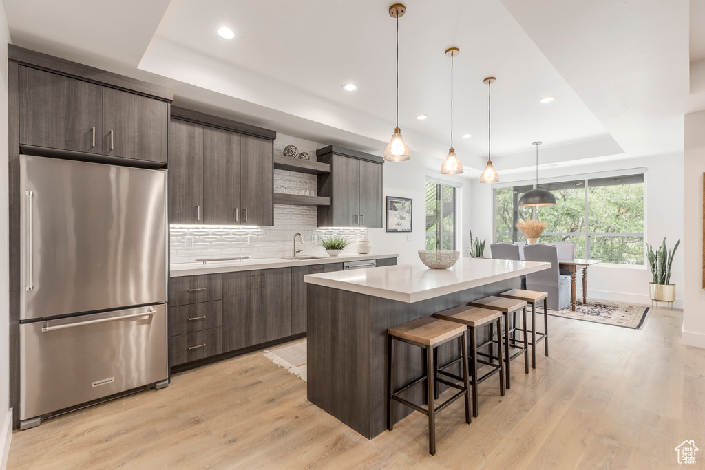 Kitchen featuring freestanding refrigerator, open shelves, a tray ceiling, light countertops, and a kitchen island