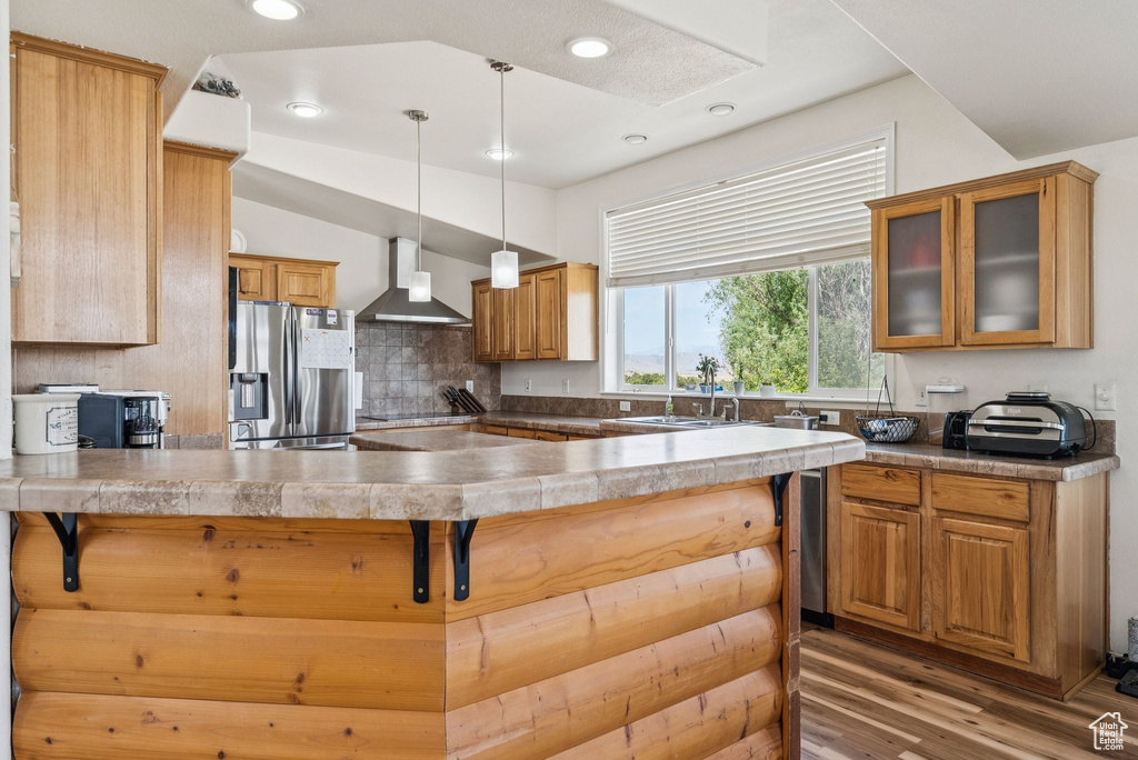 Kitchen with stainless steel fridge, wall chimney exhaust hood, a sink, a peninsula, and glass insert cabinets