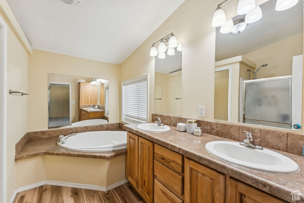 Bathroom featuring a shower stall, a bath, double vanity, wood finished floors, and vaulted ceiling