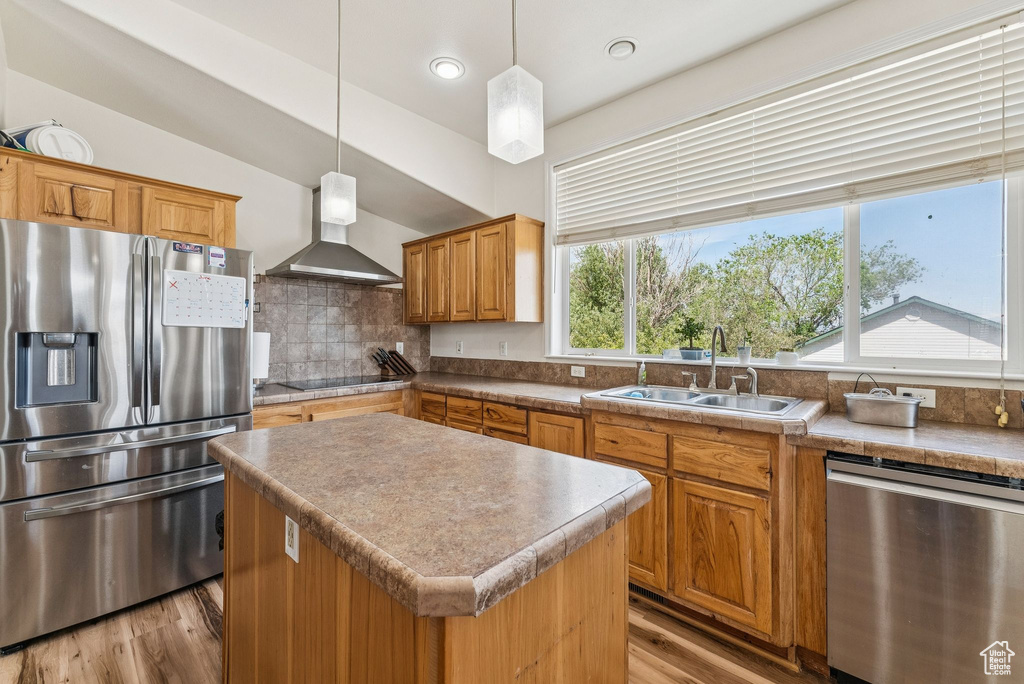 Kitchen with stainless steel appliances, wall chimney range hood, a sink, light wood-style flooring, and backsplash