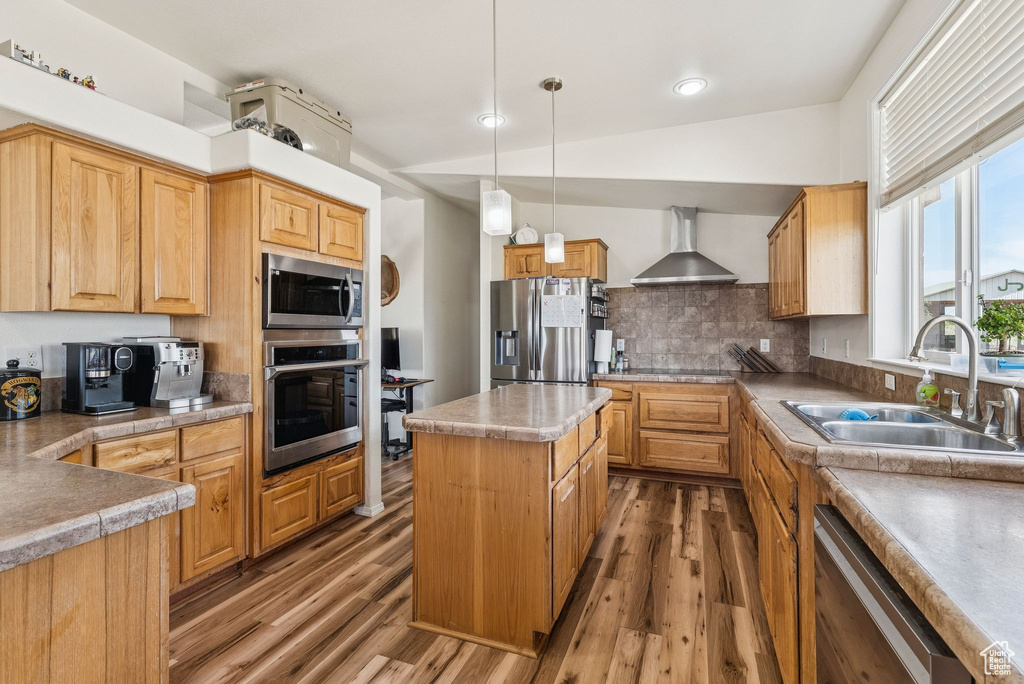 Kitchen with appliances with stainless steel finishes, wall chimney range hood, a sink, and wood finished floors