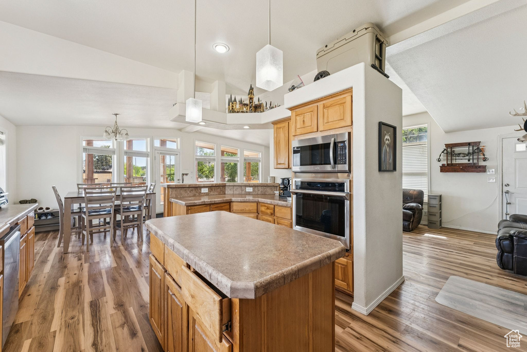 Kitchen with appliances with stainless steel finishes, vaulted ceiling, wood finished floors, a chandelier, and a peninsula
