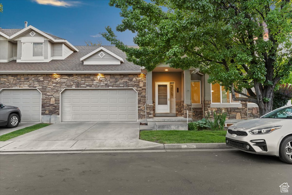 Multi unit property with stone siding, concrete driveway, a shingled roof, and an attached garage