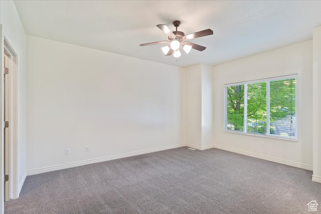 Carpeted empty room featuring ceiling fan and baseboards