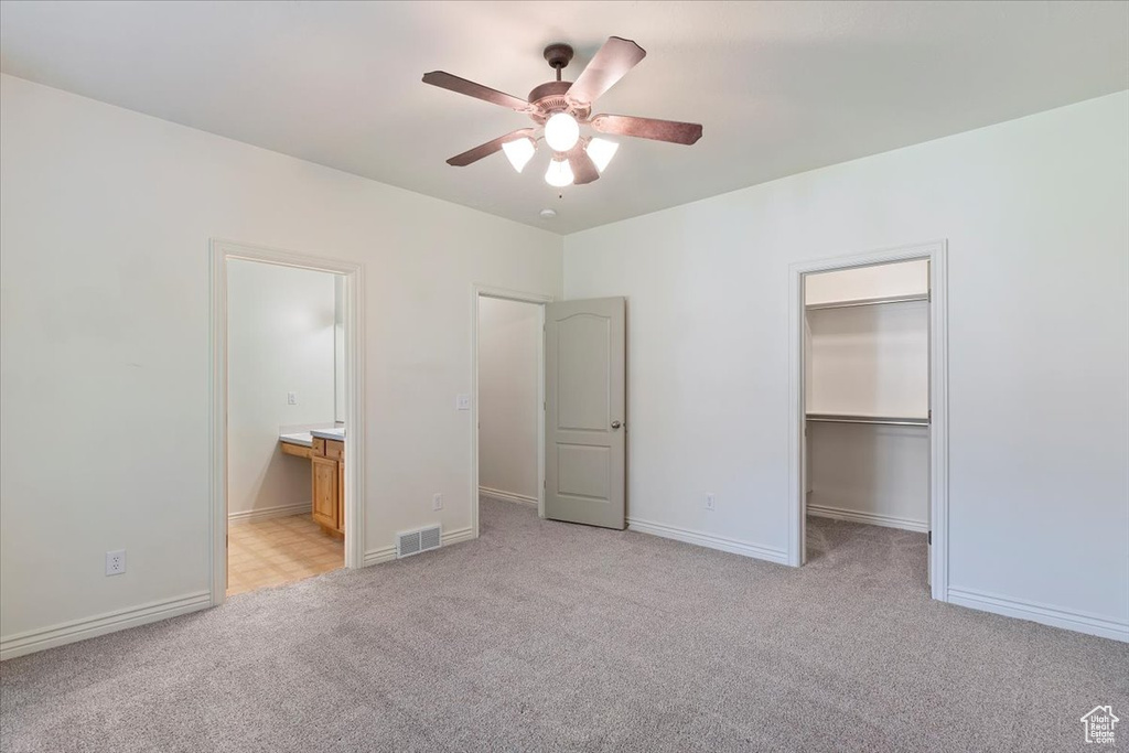 Unfurnished bedroom featuring light carpet, a walk in closet, baseboards, and connected bathroom
