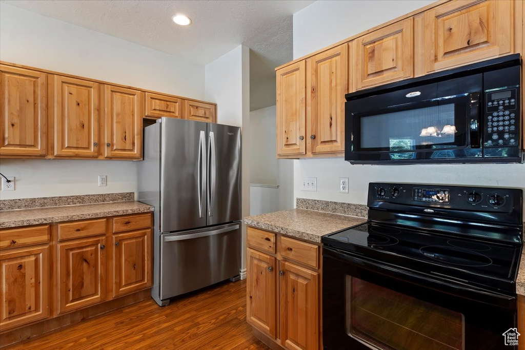 Kitchen with black appliances, dark wood finished floors, light countertops, and brown cabinetry