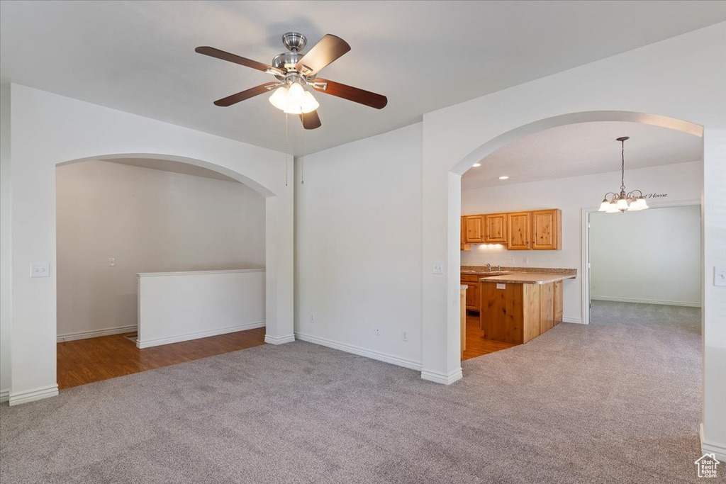 Unfurnished living room with light colored carpet, arched walkways, a ceiling fan, and baseboards