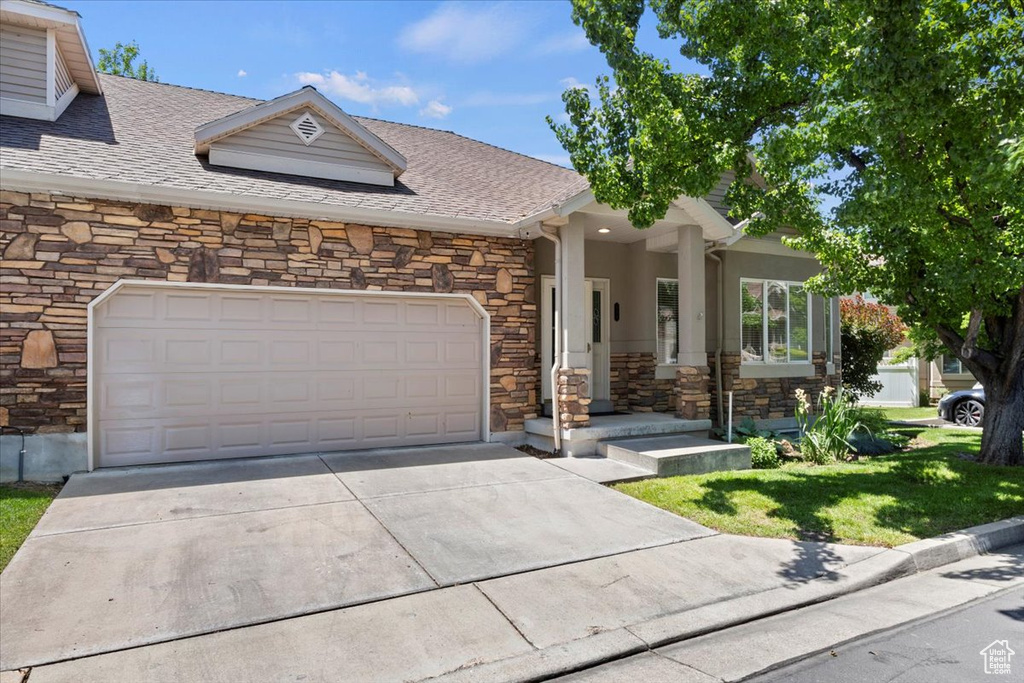View of front facade featuring stone siding, driveway, a front yard, and an attached garage