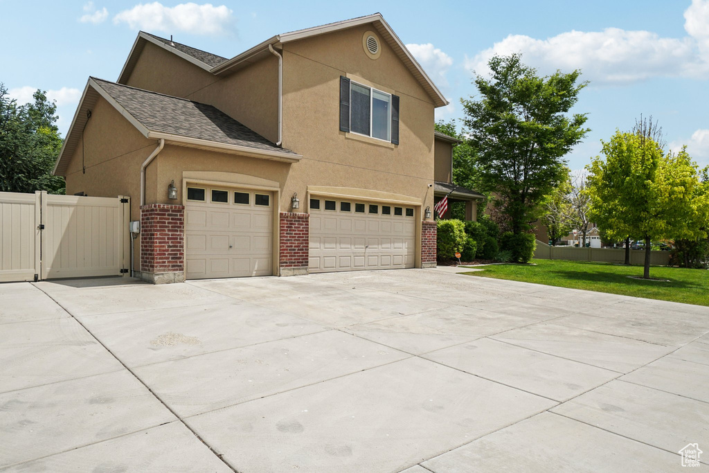 View of home's exterior featuring stucco siding, a gate, concrete driveway, brick siding, and a garage