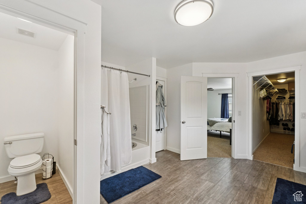 Full bath with shower / tub combo, wood finished floors, toilet, a spacious closet, and baseboards