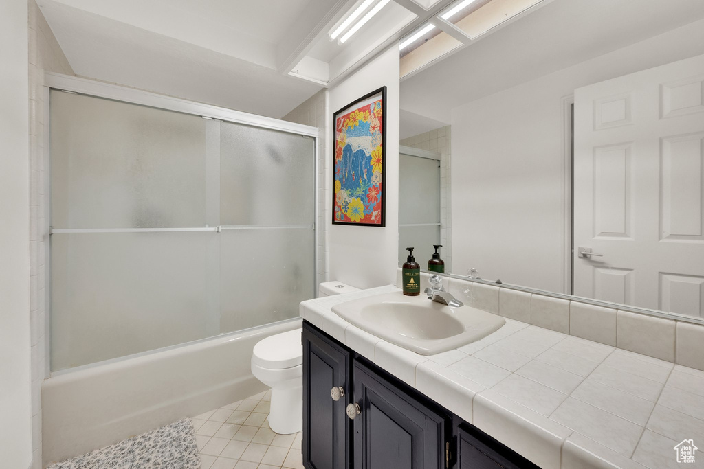 Full bath with toilet, vanity, tile patterned floors, and shower / bath combination with glass door