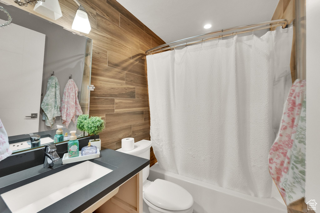 Full bath with vanity, shower / bath combo with shower curtain, wooden walls, toilet, and recessed lighting