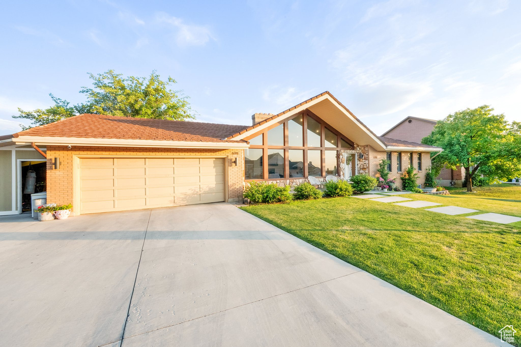 View of front facade featuring a garage, driveway, a front yard, and brick siding