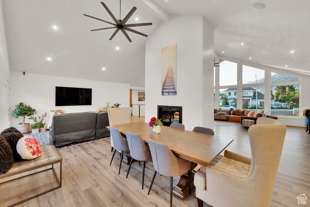 Dining space featuring high vaulted ceiling, a fireplace, a ceiling fan, light wood-type flooring, and beam ceiling