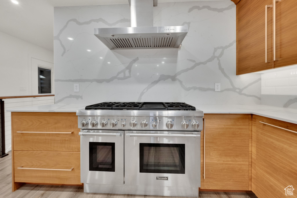 Kitchen featuring double oven range, wall chimney range hood, light stone counters, and modern cabinets