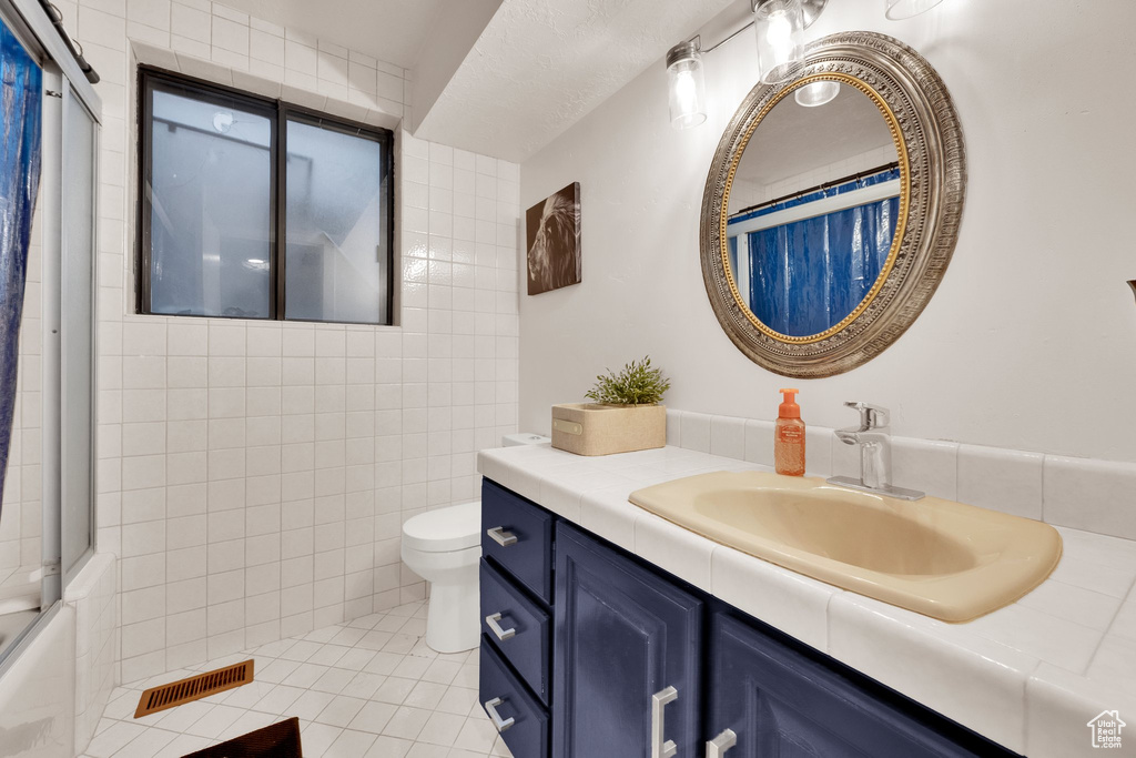 Bathroom with vanity, toilet, tile walls, tile patterned flooring, and bath / shower combo with glass door