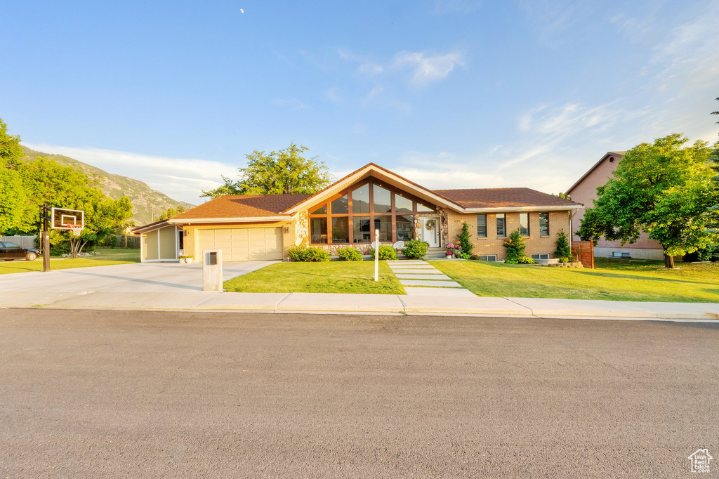 Ranch-style house featuring a garage, a front lawn, driveway, and a mountain view