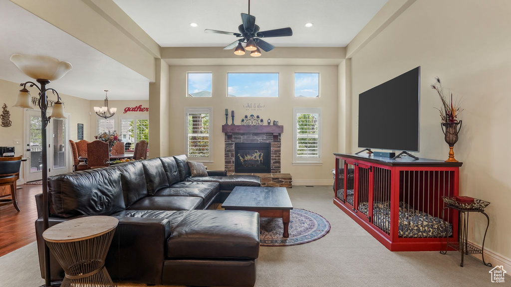 Living room featuring a stone fireplace, a chandelier, baseboards, ceiling fan, and recessed lighting