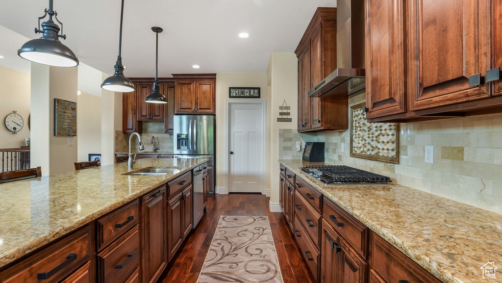Kitchen with a sink, wall chimney range hood, stainless steel appliances, dark wood-style flooring, and light stone countertops