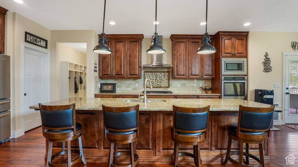 Kitchen with stainless steel appliances, a sink, tasteful backsplash, dark wood-style floors, and a center island with sink