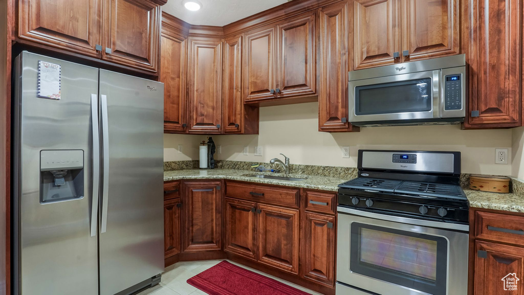 Kitchen with stainless steel appliances, a sink, light stone countertops, and light tile patterned floors